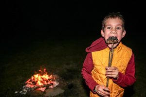 boy eating smores on stick at campfire at overnight camp